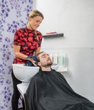 Les cheveux du client masculin de séchage de styliste en coiffure dans le salon photo libre de droits Les cheveux du client masculin de séchage de styliste en coiffure dans le salon photo libre de droits