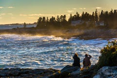 Les couples observant de grandes vagues se brisent sur des roches au coucher du soleil, chez Pemaqui photos libres de droits Les couples observant de grandes vagues se brisent sur des roches au coucher du soleil, chez Pemaqui photos libres de droits