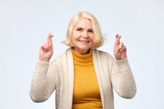 Les doigts de croisement de sourire de femme caucasienne d'Enior avec espoir et les yeux se sont fermés photo stock Les doigts de croisement de sourire de femme caucasienne d'Enior avec espoir et les yeux se sont fermés photo stock