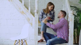 Les jeunes couples heureux et affectueux boivent le thé et parler tout en se reposant sur des escaliers dans le salon à la maison images libres de droits Les jeunes couples heureux et affectueux boivent le thé et parler tout en se reposant sur des escaliers dans le salon à la maison images libres de droits