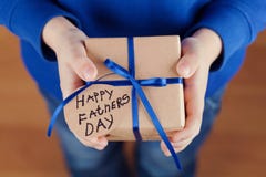 Les mains des enfants tenant un cadeau ou une boîte actuelle avec le papier d'emballage et l'étiquette attachée de ruban bleu le photographie stock Les mains des enfants tenant un cadeau ou une boîte actuelle avec le papier d'emballage et l'étiquette attachée de ruban bleu le photographie stock