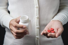 Les mains femelles tient une bouteille de pilule blanche et des pilules rouges dans le hea photos stock Les mains femelles tient une bouteille de pilule blanche et des pilules rouges dans le hea photos stock