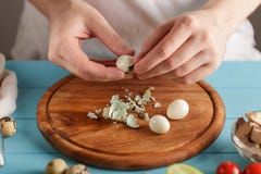 Les mains masculines épluche les oeufs de caille bouillis de la coquille sur la planche à découper en bois dans la cuisine photo stock Les mains masculines épluche les oeufs de caille bouillis de la coquille sur la planche à découper en bois dans la cuisine photo stock