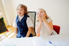 Les petits écoliers drôles, garçon et fille, s'asseyent à un bureau photographie stock Les petits écoliers drôles, garçon et fille, s'asseyent à un bureau photographie stock