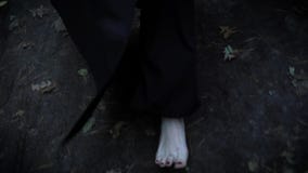 Les pieds pâles nus de la femme porte le long manteau noir, marchant dans la forêt en automne au-dessus de la terre humide et des Les pieds pâles nus de la femme porte le long manteau noir, marchant dans la forêt en automne au-dessus de la terre humide et des