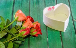Les roses oranges et rouges fleurit avec le boîte-cadeau de forme de coeur, fond en bois vert Photo libre de droits