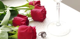 Les roses rouges s'étendent sur la table blanche près de l'anneau argenté avec le grand diamant clair images stock Les roses rouges s'étendent sur la table blanche près de l'anneau argenté avec le grand diamant clair images stock