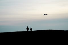 Les silhouettes du support de deux personnes sur une haute colline et observer une haute de vol d'avion dans le ciel photo libre de droits Les silhouettes du support de deux personnes sur une haute colline et observer une haute de vol d'avion dans le ciel photo libre de droits