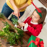 Leuk kleutermeisje rendiergeweitakken dragen en haar moeder die Kerstmiskroon in woonkamer maken De pret van de Kerstmisfamilie royalty-vrije stock fotografie Leuk kleutermeisje rendiergeweitakken dragen en haar moeder die Kerstmiskroon in woonkamer maken De pret van de Kerstmisfamilie royalty-vrije stock fotografie