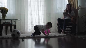 Leuke baby die op de vloer bij het pluizige tapijt spelen met binnen ballen en ballon kruipen terwijl zijn jonge moederzitting stock videobeelden Leuke baby die op de vloer bij het pluizige tapijt spelen met binnen ballen en ballon kruipen terwijl zijn jonge moederzitting stock videobeelden