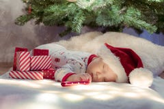 Leuke pasgeboren babyslaap onder Kerstboom dichtbij rode giften die Santa Claus-hoed dragen stock foto's Leuke pasgeboren babyslaap onder Kerstboom dichtbij rode giften die Santa Claus-hoed dragen stock foto's