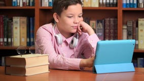 Leuke schooljongen gebruikend computertablet en luisterend aan het lezing stock video Leuke schooljongen gebruikend computertablet en luisterend aan het lezing stock video