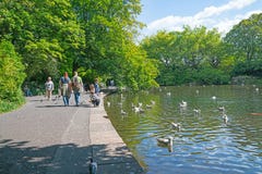 Leute genießen, um Teich zu gehen, während Kinder Enten einziehen lizenzfreies stockbild Leute genießen, um Teich zu gehen, während Kinder Enten einziehen lizenzfreies stockbild