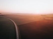 Lever de soleil brumeux au-dessus de la route entourée par des champs d'agriculture Automne tôt photographie stock Lever de soleil brumeux au-dessus de la route entourée par des champs d'agriculture Automne tôt photographie stock