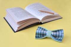 Libro aperto, una cravatta a farfalla e una matita di legno su un fondo giallo con lo spazio della copia immagine stock Libro aperto, una cravatta a farfalla e una matita di legno su un fondo giallo con lo spazio della copia immagine stock