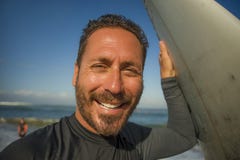 Lifestyle beach closeup portrait of handsome and attractive surfer man in neoprene swimsuit holding surf board posing cool after royalty free stock photos Lifestyle beach closeup portrait of handsome and attractive surfer man in neoprene swimsuit holding surf board posing cool after royalty free stock photos