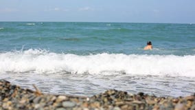 Lifestyle man walks into the sea on a pebble beach and swims on the wave. stock video Lifestyle man walks into the sea on a pebble beach and swims on the wave. stock video
