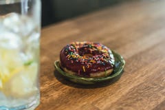 Limonade froide avec de la glace et des citrons dans un verre grand avec un tube jetable Beignet de chocolat avec le habillage image libre de droits Limonade froide avec de la glace et des citrons dans un verre grand avec un tube jetable Beignet de chocolat avec le habillage image libre de droits