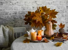 Lit candles, dry maple leaves, pumpkin, stack of books - autumn still life interior decoration house. Cozy home concept