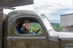 lite deltar pojken i form av en sovjetisk soldat i cockpiten av en armébil i en ståta i heder av segerdagen Royaltyfri Bild lite deltar pojken i form av en sovjetisk soldat i cockpiten av en armébil i en ståta i heder av segerdagen Royaltyfri Bild
