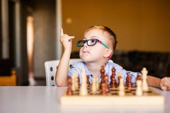 Little baby boy with down syndrome with big blue glasses playing chess in kindergarten stock photo Little baby boy with down syndrome with big blue glasses playing chess in kindergarten stock photo