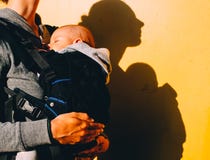 Little baby in carrier and mother with prize on yellow background stock photo Little baby in carrier and mother with prize on yellow background stock photo