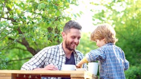 Little boy and handsome Father having breakfast in the garden. Parenthood. Food and Drink for family. Happy father with stock footage Little boy and handsome Father having breakfast in the garden. Parenthood. Food and Drink for family. Happy father with stock footage