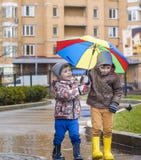 Little boy playing in rainy summer park. Child with colorful rainbow umbrella, waterproof coat and boots jumping in puddle and mud Royalty Free Stock Photos Little boy playing in rainy summer park. Child with colorful rainbow umbrella, waterproof coat and boots jumping in puddle and mud Royalty Free Stock Photos