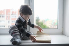 The little boy is reading a book. The child sits at the window a royalty free stock images The little boy is reading a book. The child sits at the window a royalty free stock images