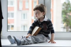 The little boy is reading a book. The child sits at the window a royalty free stock image The little boy is reading a book. The child sits at the window a royalty free stock image