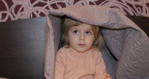 Little cheerful girl hides under blanket and watching TV. Concept of kids sleep stock images Little cheerful girl hides under blanket and watching TV. Concept of kids sleep stock images