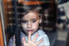 Little crying girl standing behind the glass door and looking for parents. Sad child royalty free stock photo Little crying girl standing behind the glass door and looking for parents. Sad child royalty free stock photo