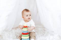 Little Cute Baby Girl With A Toy Pyramid Sitting In White Interior At Home. Stock Photo Little Cute Baby Girl With A Toy Pyramid Sitting In White Interior At Home. Stock Photo