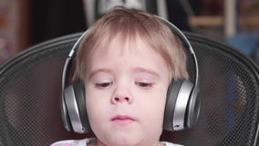 A little funny boy sits in a chair and listens to music through headphones. Face close up stock video footage A little funny boy sits in a chair and listens to music through headphones. Face close up stock video footage
