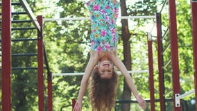Little funny girl hanging upside down on the horizontal bar.