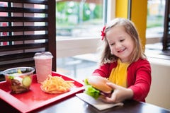 Little girl eating a hamburger in fast food restaurant Royalty Free Stock Images Little girl eating a hamburger in fast food restaurant Royalty Free Stock Images