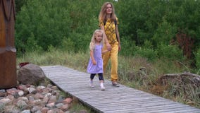 Little girl jump off big stone and walk with her mother through wooden path stock video footage Little girl jump off big stone and walk with her mother through wooden path stock video footage