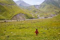 A little girl in a red dress and a knitted cap-strawberry runs on a green field in the mountains. stock photo A little girl in a red dress and a knitted cap-strawberry runs on a green field in the mountains. stock photo