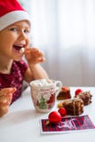 Little girl in Santa hat eating marshmallow from mug with cacao and cookies, Merry Cristmas stock photography Little girl in Santa hat eating marshmallow from mug with cacao and cookies, Merry Cristmas stock photography
