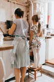 Little girl staying on the stool next to her mother is cooking pancakes for the breakfast in the little cozy kitchen royalty free stock image Little girl staying on the stool next to her mother is cooking pancakes for the breakfast in the little cozy kitchen royalty free stock image