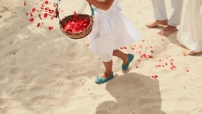 A little girl throws petals of red roses at the feet of the newlyweds. Wedding on the tropical coast. Philippines.