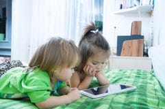 Little girls looking on pad lying on bed at home. Children time spending stock photos Little girls looking on pad lying on bed at home. Children time spending stock photos