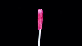 Lollipop heart on a stick on a black background. The caramel candy is spinning
