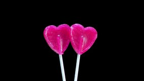 Lollipop two hearts on a stick on a black background. The caramel candy is spinning