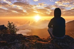 Lonely Man sitting on a mountain for watching Sunrise views alone,success and peace concept in warm
