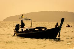 Long bateau thaïlandais et un kayak en mer au coucher du soleil, avec des couleurs d'or, en plage de Railay, Krabi, Thaïlande image stock Long bateau thaïlandais et un kayak en mer au coucher du soleil, avec des couleurs d'or, en plage de Railay, Krabi, Thaïlande image stock