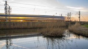 Long exposure train with setting sun shining through the train on Dutch traintrack.