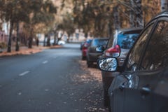 Long row of different shiny cars and vans parked along empty roadside on sunny autumn day on blurred green golden foliage bokeh stock photos Long row of different shiny cars and vans parked along empty roadside on sunny autumn day on blurred green golden foliage bokeh stock photos