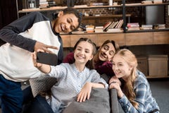 Los adolescentes multiculturales felices agrupan tomar el selfie en smartphone y sentarse en el sofá en casa imagenes de archivo Los adolescentes multiculturales felices agrupan tomar el selfie en smartphone y sentarse en el sofá en casa imagenes de archivo