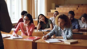 Los estudiantes cansados y aburridos están escuchando el profesor y están haciendo notas en los cuadernos que se sientan en los e almacen de video Los estudiantes cansados y aburridos están escuchando el profesor y están haciendo notas en los cuadernos que se sientan en los e almacen de video
